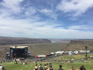 alt="crowd of people on hill overlooking a large stage with The Gorge in background"