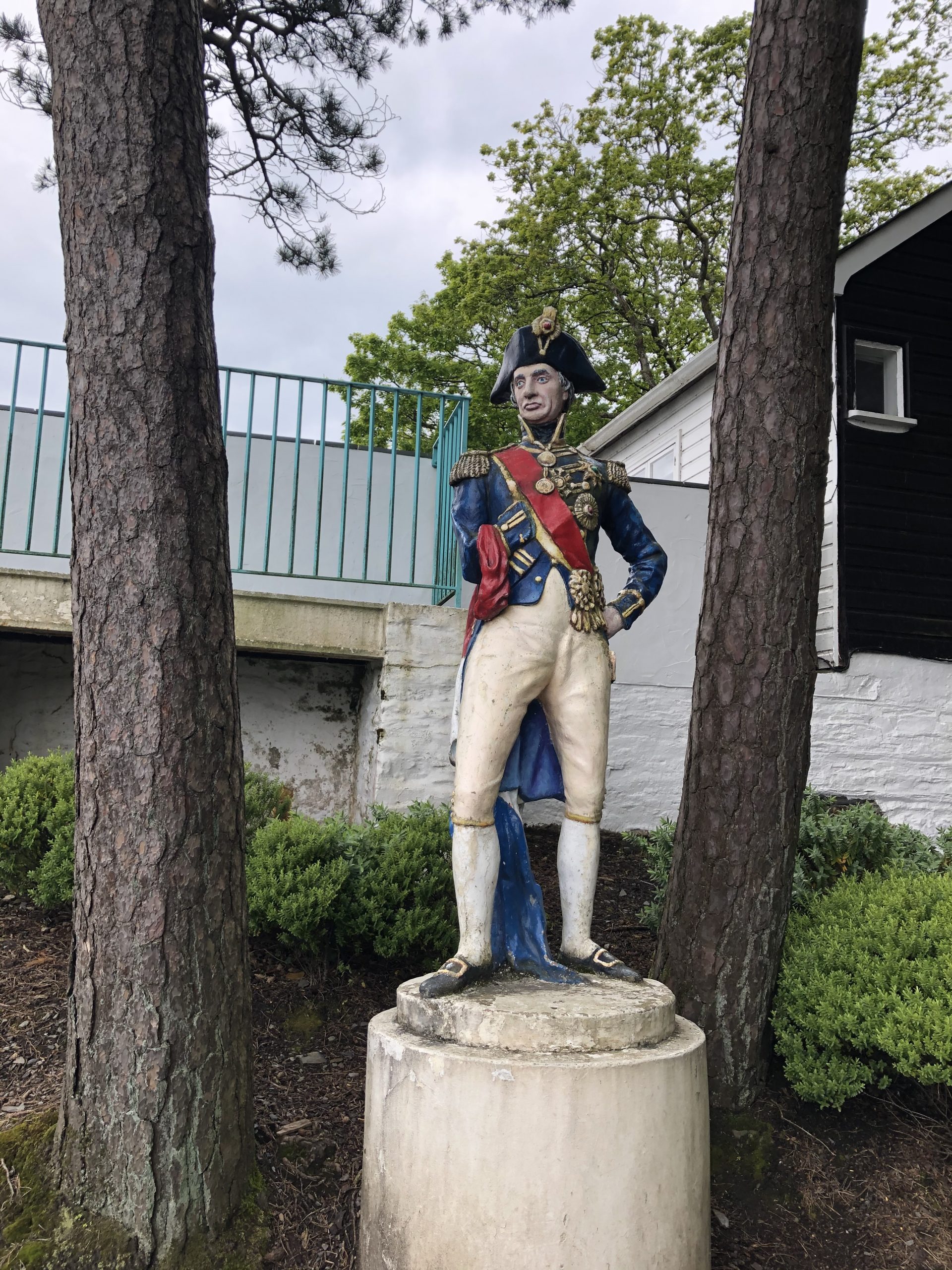 alt="statue of man in old style naval uniform between two trees"