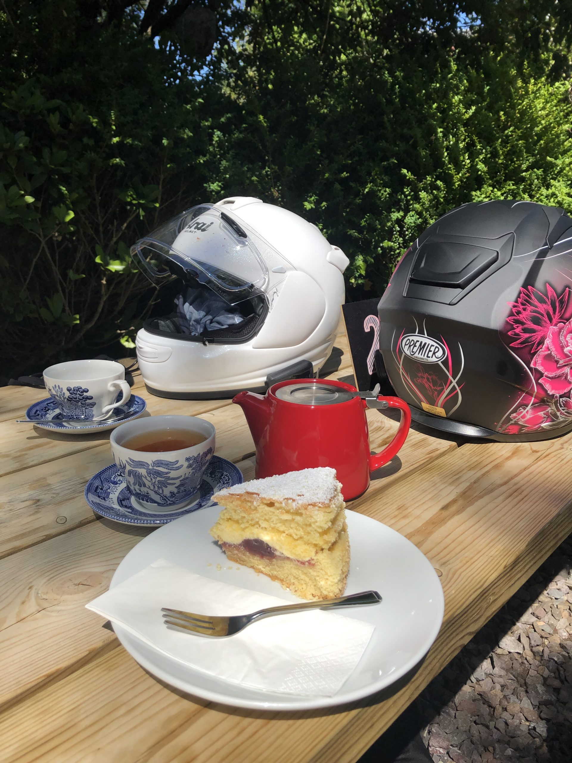 alt="cream cake & cups of tea beside two motorbike helmets"