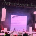 alt="computer generated images behind band on stage"