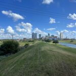alt="green mound with city buildings in distance"