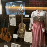 alt="glass cabinet with a dress & guitars inside"