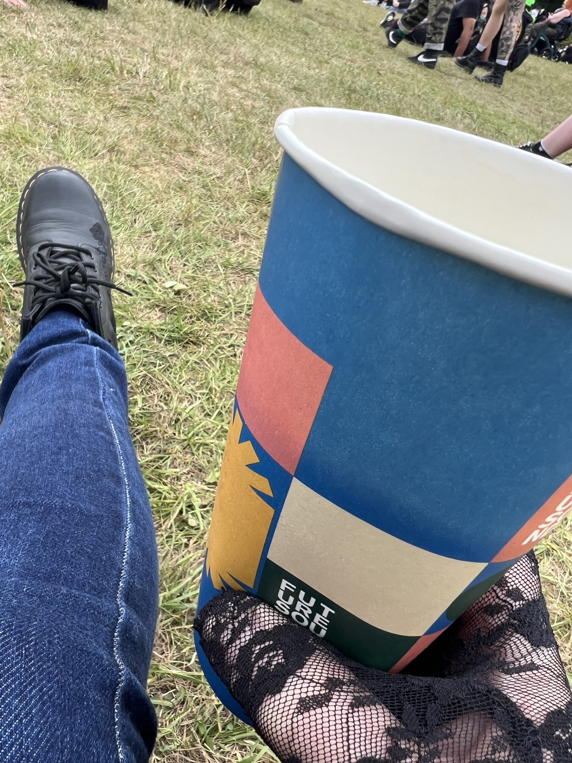 alt="a leg with doc marten boot on & hand holding paper cup"