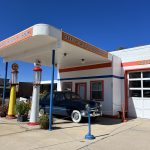 al="old fashioned car next to an old petrol pump"