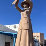 alt="statue of a woman with large hat holding leaves"