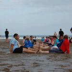 alt="sandy beach with people sat in two rows"