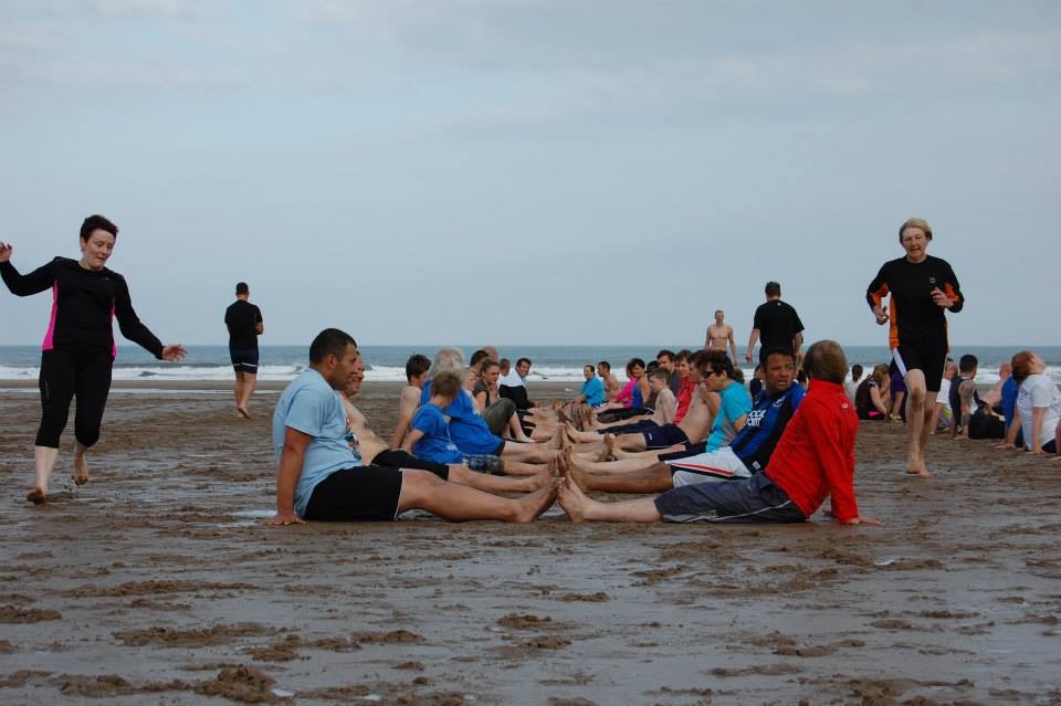 alt="sandy beach with people sat in two rows"