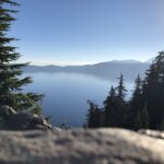 alt="pine trees with lake & mountains in the mist"