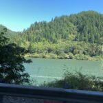 alt="river with pine tree covered hill in background"