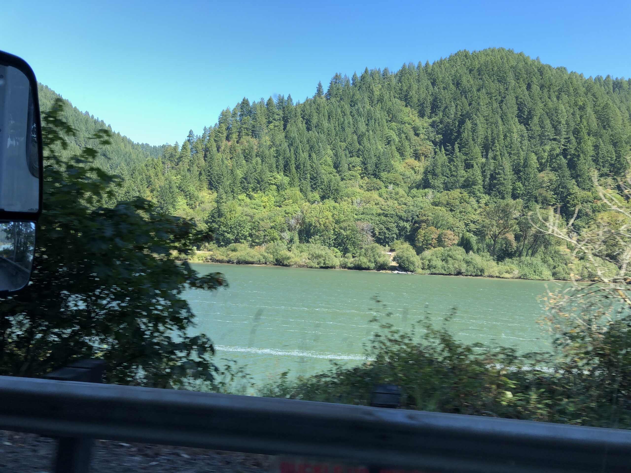 alt="river with pine tree covered hill in background"