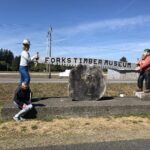 alt="the two figures holding a saw outside Forks museum"