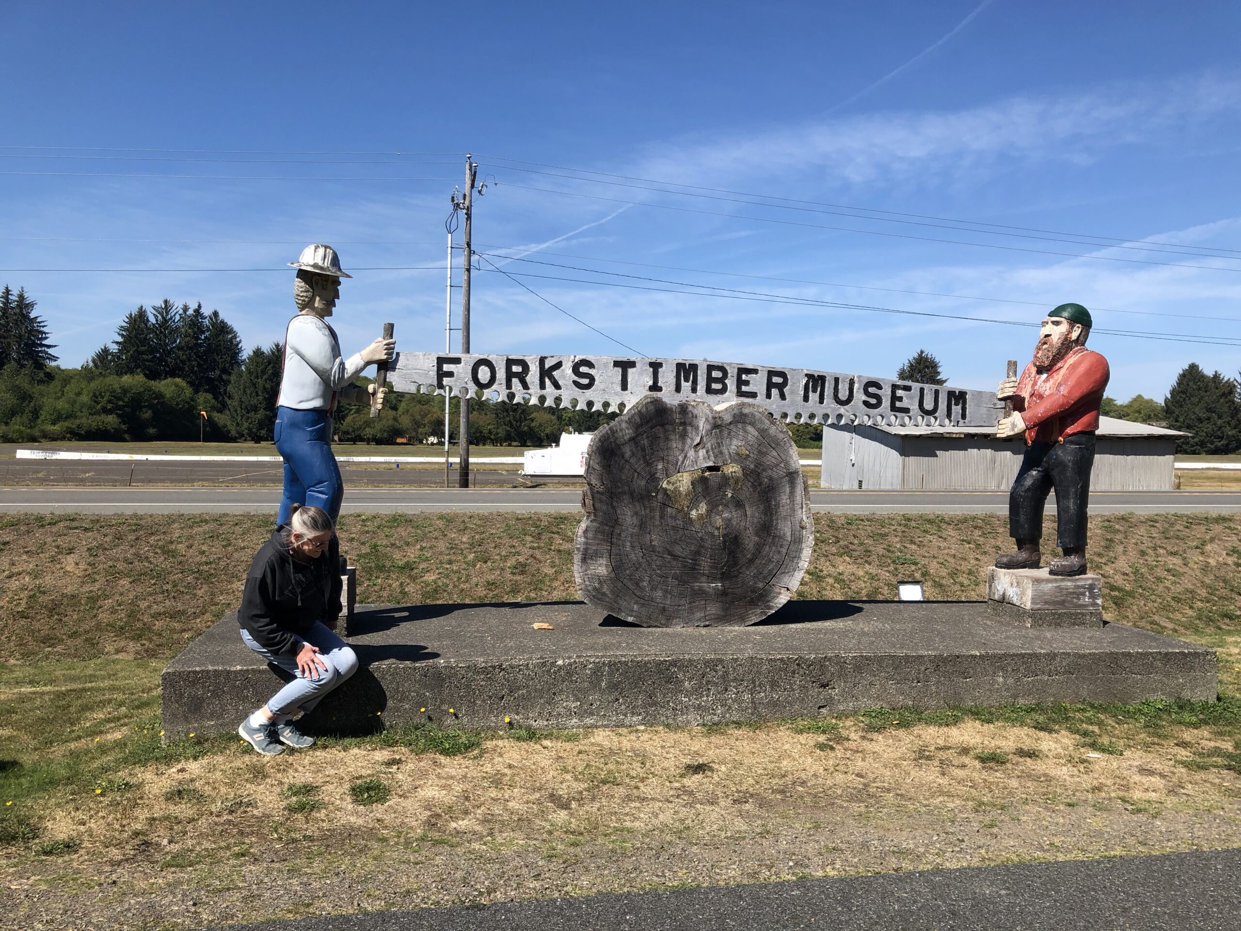 alt="the two figures holding a saw outside Forks museum"