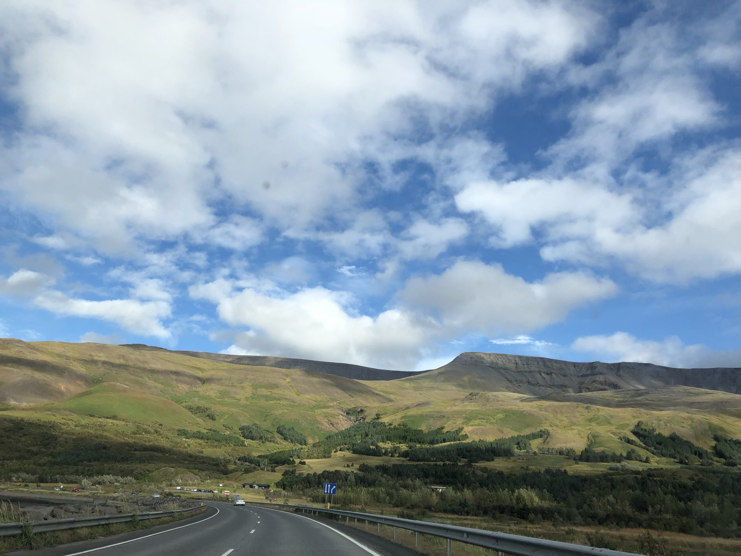alt="open grass land & mountain in front with cloudy sky above"