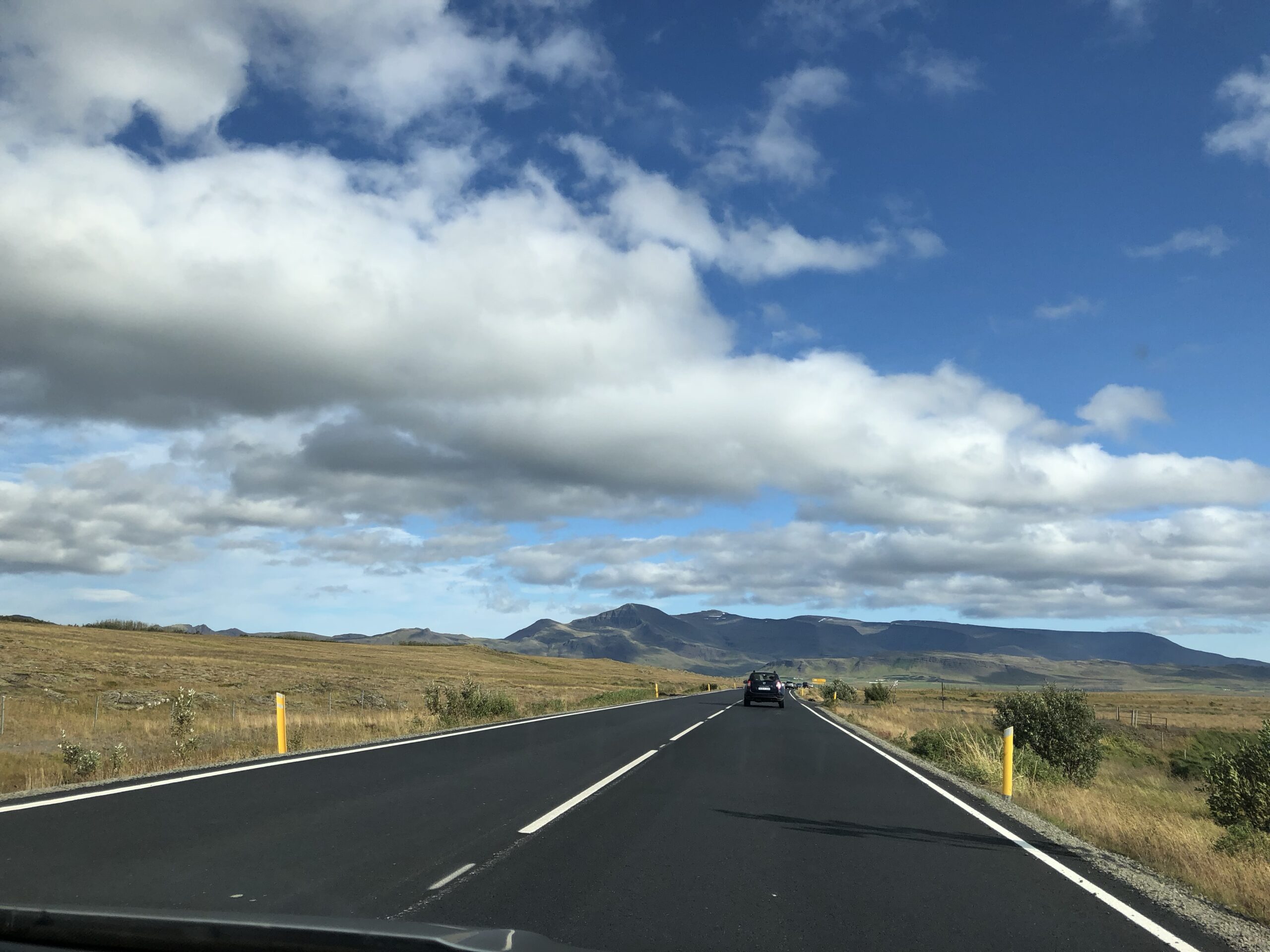 alt="straight road with grass land either side of the& mountains in distance"