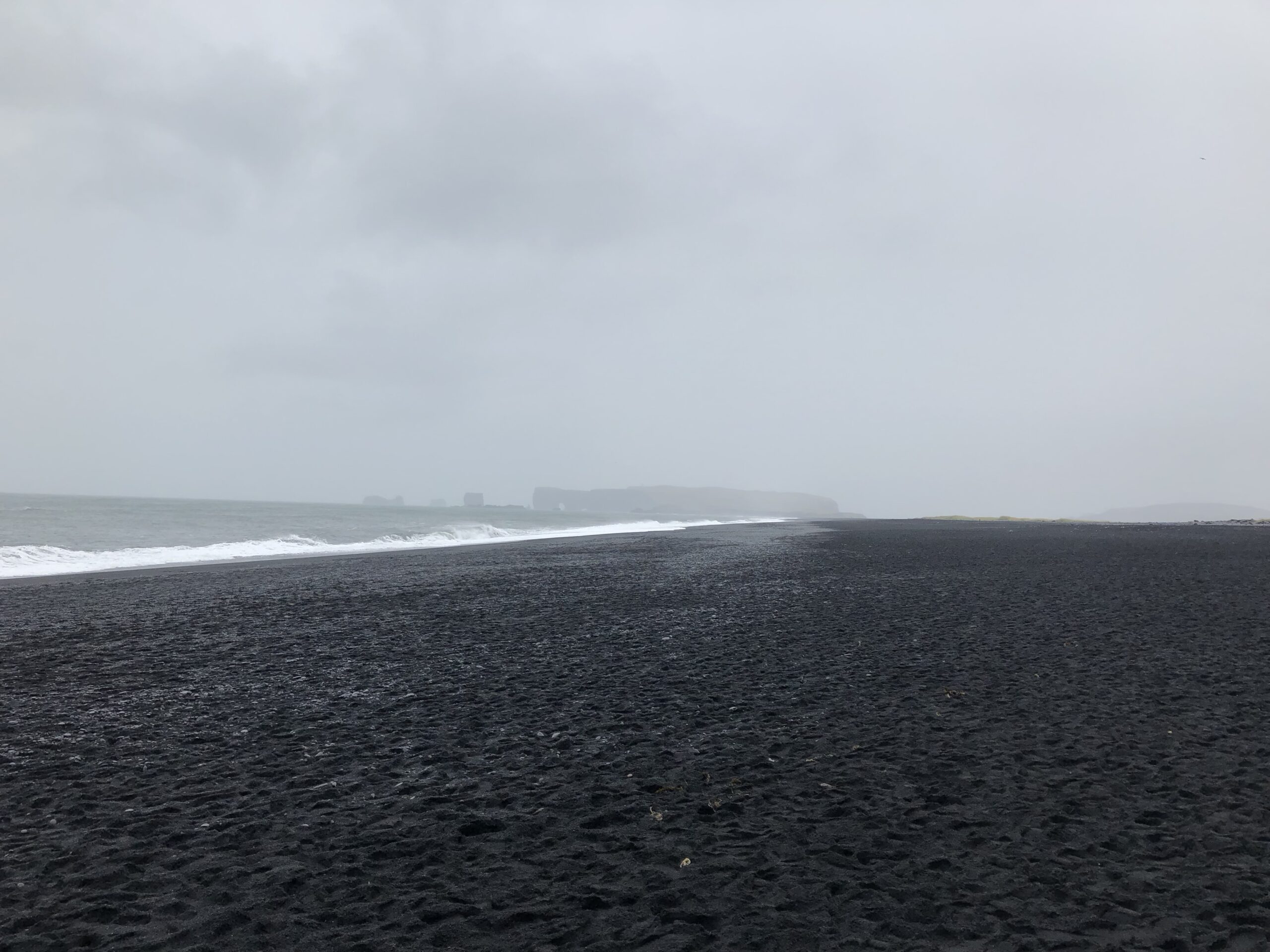 alt="wide expanse of dark sand beach with sea"