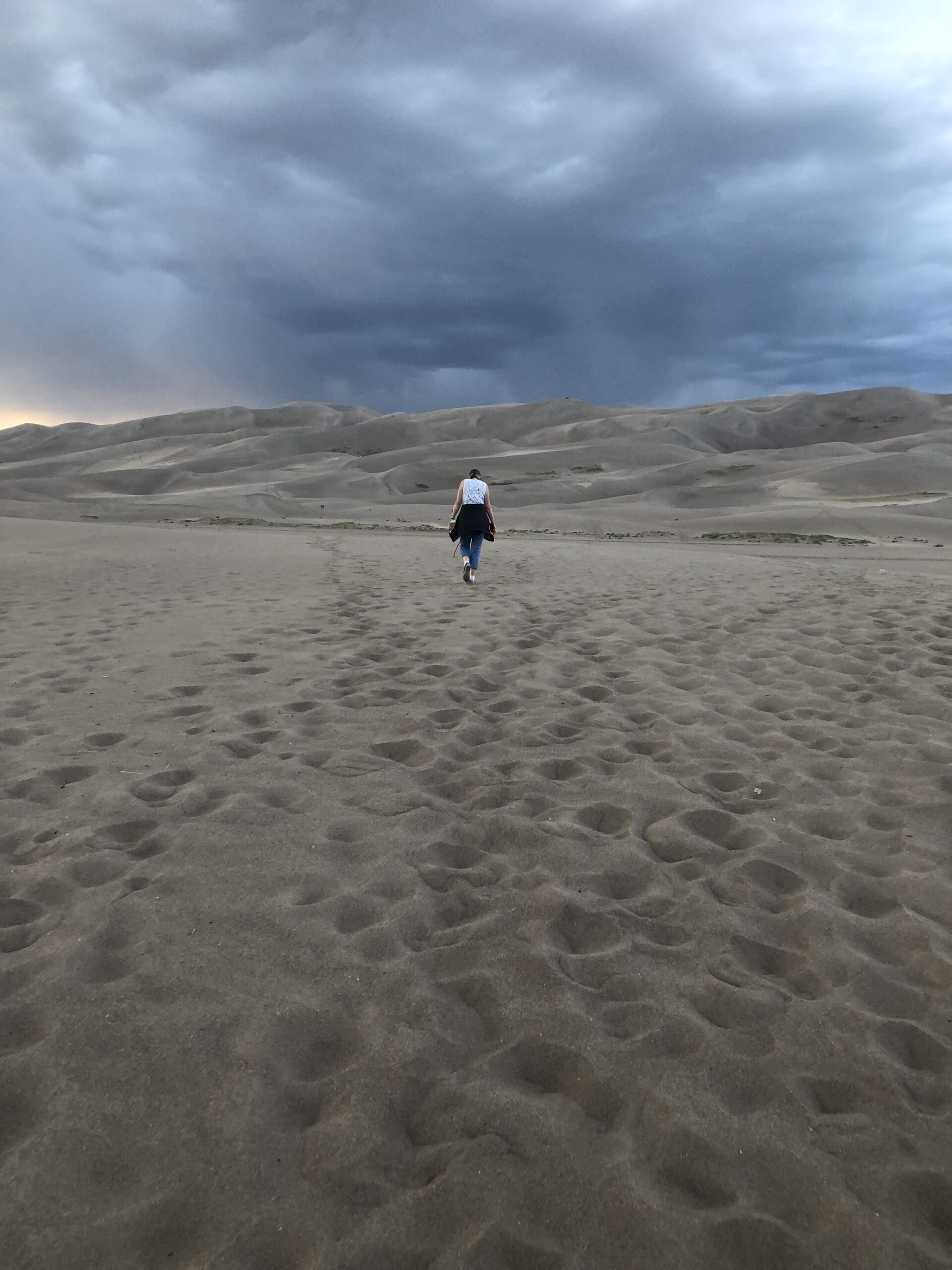 alt="person walking towards sand dune"