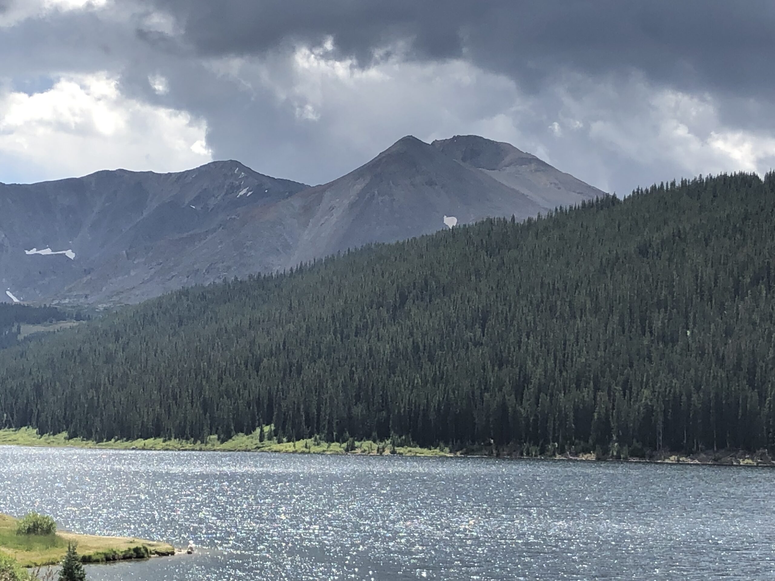 alt="water with tree covered hill & mountains in background"